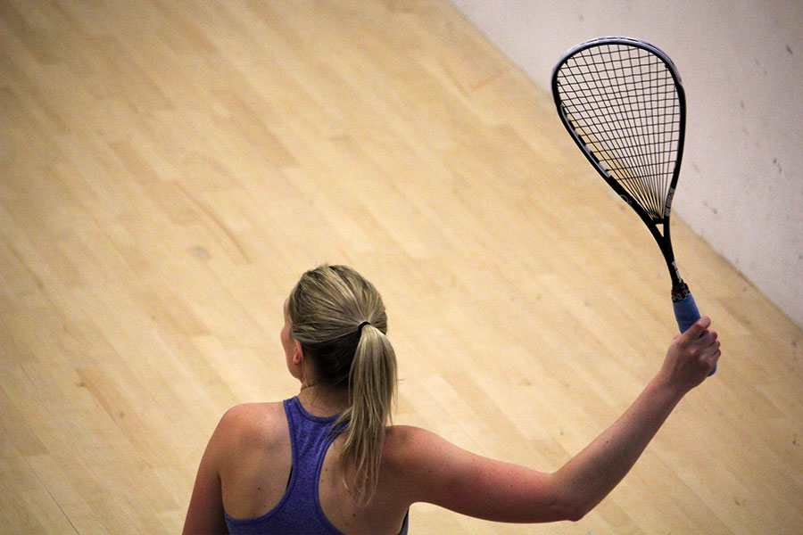 Female competitive squash player hitting a smash.